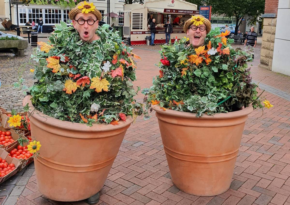 Two men pulling silly faces dressed up as vines in flower pots